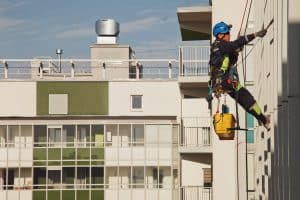 Industrial mountaineering worker hangs over residential building while washing exterior facade glazing